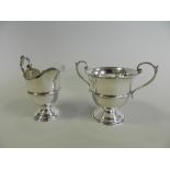 A silver cream jug together with a silver sugar bowl in the form of a trophy cup,