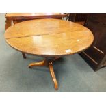 An early 19th century oak tilt top tripod table on turned baluster column,