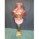 A brass Corinthian column oil lamp with opaque pink glass reservoir and cranberry shade