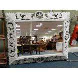 An Indian wall mirror in canted foliate carved frame centred by a wheel,