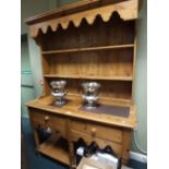A modern pine kitchen dresser with shaped canopied rack over two shelves and two drawers,