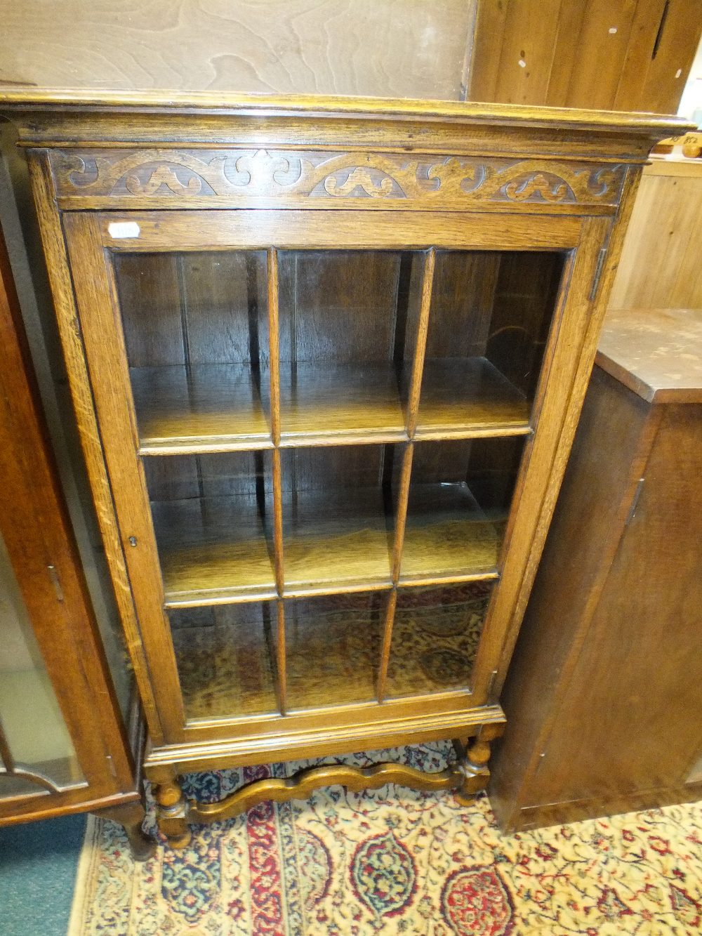 An oak single door display cabinet with foliate blind fret frieze above a ribbed nine pane glazed