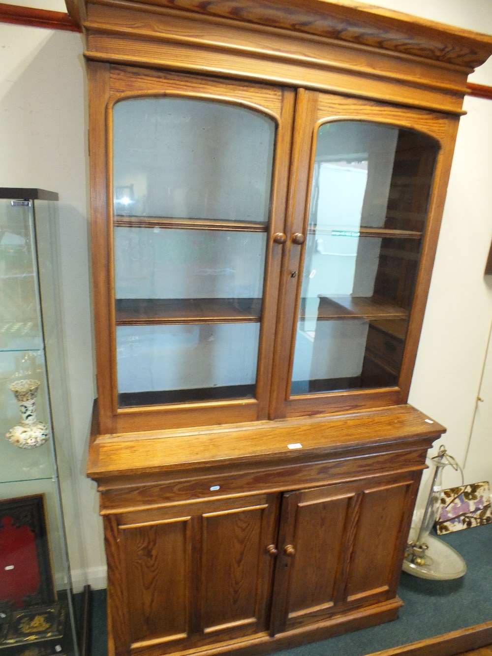 A Victorian pitch pine kitchen cabinet with moulded cornice above two arched glazed doors enclosing