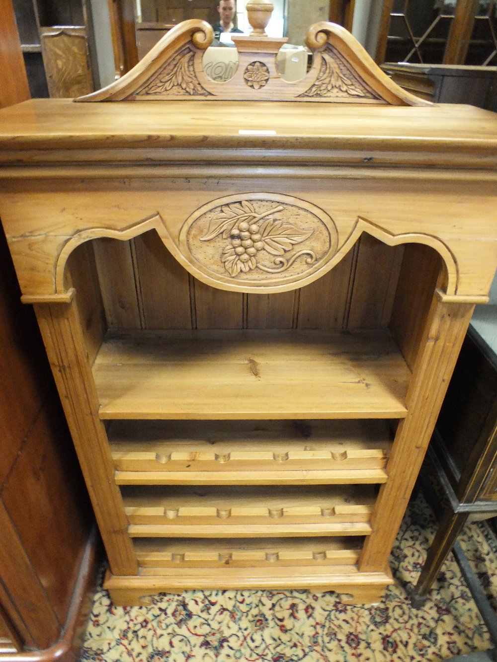 A modern pine kitchen wine rack with broken scroll pediment above shaped canopy and bottle shelf