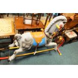 A plastic rocking horse with leather tack on a red metal trestle base