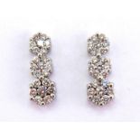 A pair of diamond triple daisy cluster ear studs, composed of three conjoined graduating clusters,