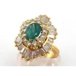 An emerald and diamond ballerina cluster dress ring, the central oval cut stone 8.6 x 6.9 above a