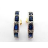 A pair of sapphire and diamond ear hoops, each channel set with alternate oval cut sapphires and