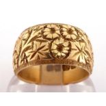 An early 20th century 18 carat gold wedding band, ornately chased with flowers amongst foliage,