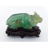 A Chinese green fluorite carving of recumbent water buffalo with wood stand, carved with legs tucked