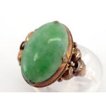 A jade ring, the oval cabochon stone 15.4 x 9.8mm, to fleur de lys shoulders, the shank stamped '
