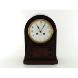 A domed top mahogany eight day mantel clock striking on a gong, the white enamel dial under domed