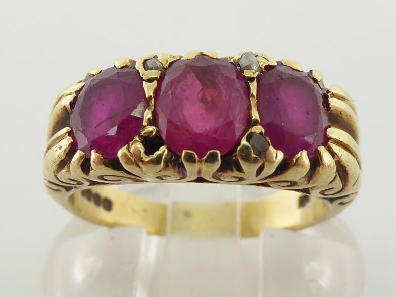 An 18 carat gold and ruby ring, the three oval cut stones claw set to a raised scroll mount, the - Image 2 of 5