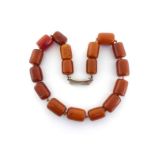 An amber bead necklace, composed of barrel shaped beads, to a white metal waisted clasp, stamped '