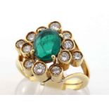 An emerald and diamond cluster ring, the central oval cut 8.4 x 6.6 x 3.2mm, in a surround of deep