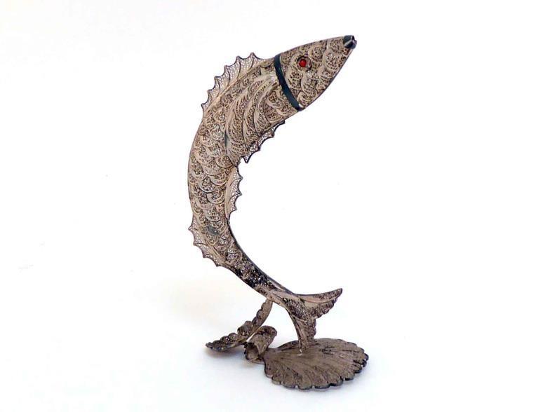 A silver filigree ornament of a leaping salmon, with red glass eyes, on shell-shaped base,