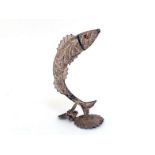 A silver filigree ornament of a leaping salmon, with red glass eyes, on shell-shaped base,