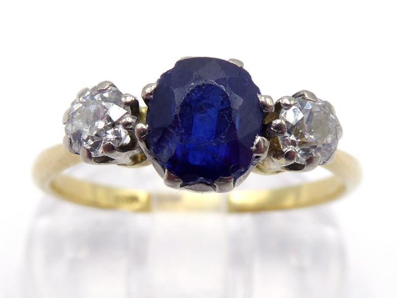 A sapphire and diamond three stone ring, the central oval cut stone 6 x 5mm, claw set between two