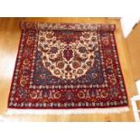 A Persian Isfahan carpet, the central stylised floral design on a deep red ground around a