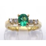 An emerald and diamond ring, the central oval cut emerald 4.5 x 5.5mm, between two pairs of