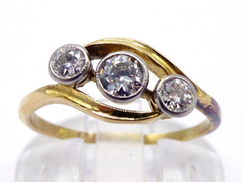 A three stone diamond ring, the three graduated old cut brilliants obliquely set in rub over mounts,