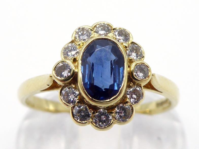 An 18 carat gold, sapphire and diamond cluster ring, the central oval cut sapphire 4 x 6 x 2.4mm, in