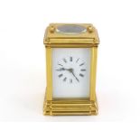 A brass-cased carriage clock with black Roman numerals on the white face, oval escapement view panel