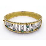 A French 14 carat gold, emerald and diamond hinged bangle, the front composed of bars set above with