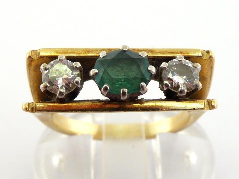 An emerald and diamond ring, the central oval cut emerald flanked by two brilliants, totalling