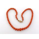 A graduated coral bead necklace, composed of 11.5 to 6mm beads, to a gold (tests 14 carat) foliate