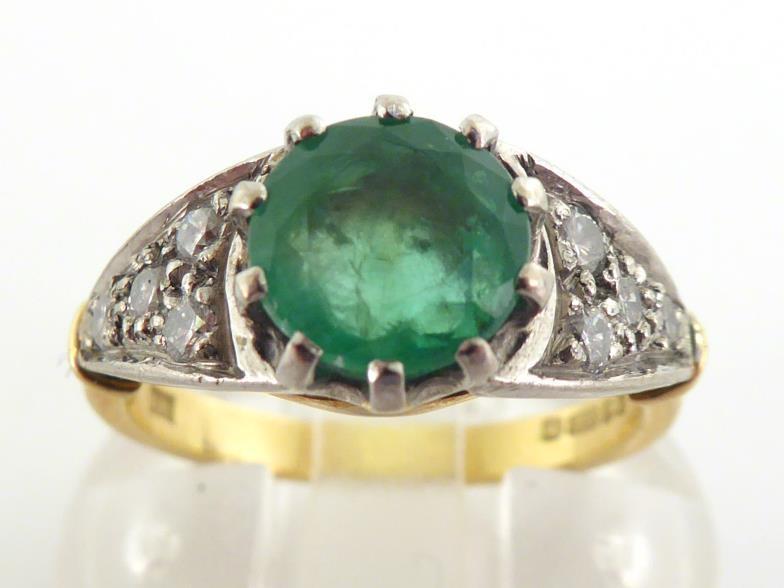 An 18 carat gold, emerald and diamond ring, the central round cut stone 7.2 x 4.5mm, claw set