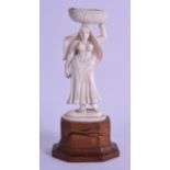 A 19TH CENTURY ANGLO INDIAN CARVED IVORY FIGURE OF A FEMALE modelled holding aloft a basket of