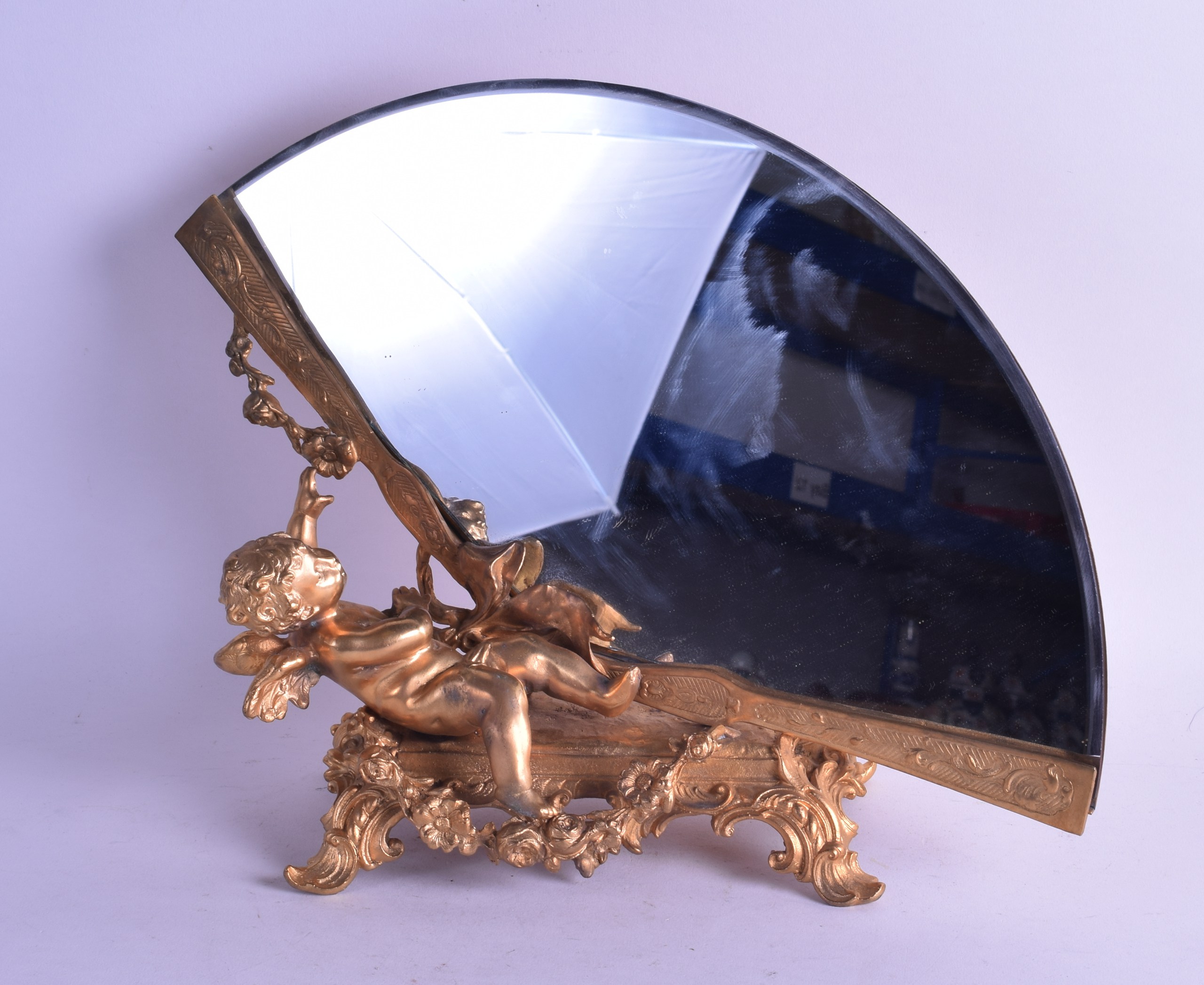 A CONTEMPORARY ORMOLU FAN SHAPED MIRROR depicting a leaning cherub. 32 cm x 28 cm. Minor tarnishing