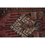 A RED GROUND PERSIAN RUG, decorated with motifs and symbols. 192 cm x 99 cm.