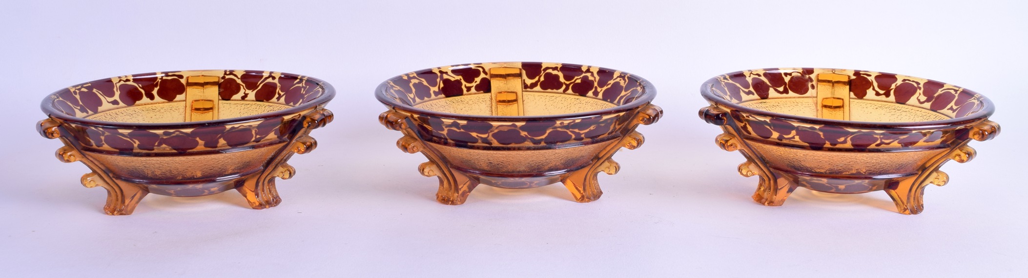 A SET OF THREE ART DECO SMOKEY AMBER AND RUBY GLASS BOWLS with angular supports and floral