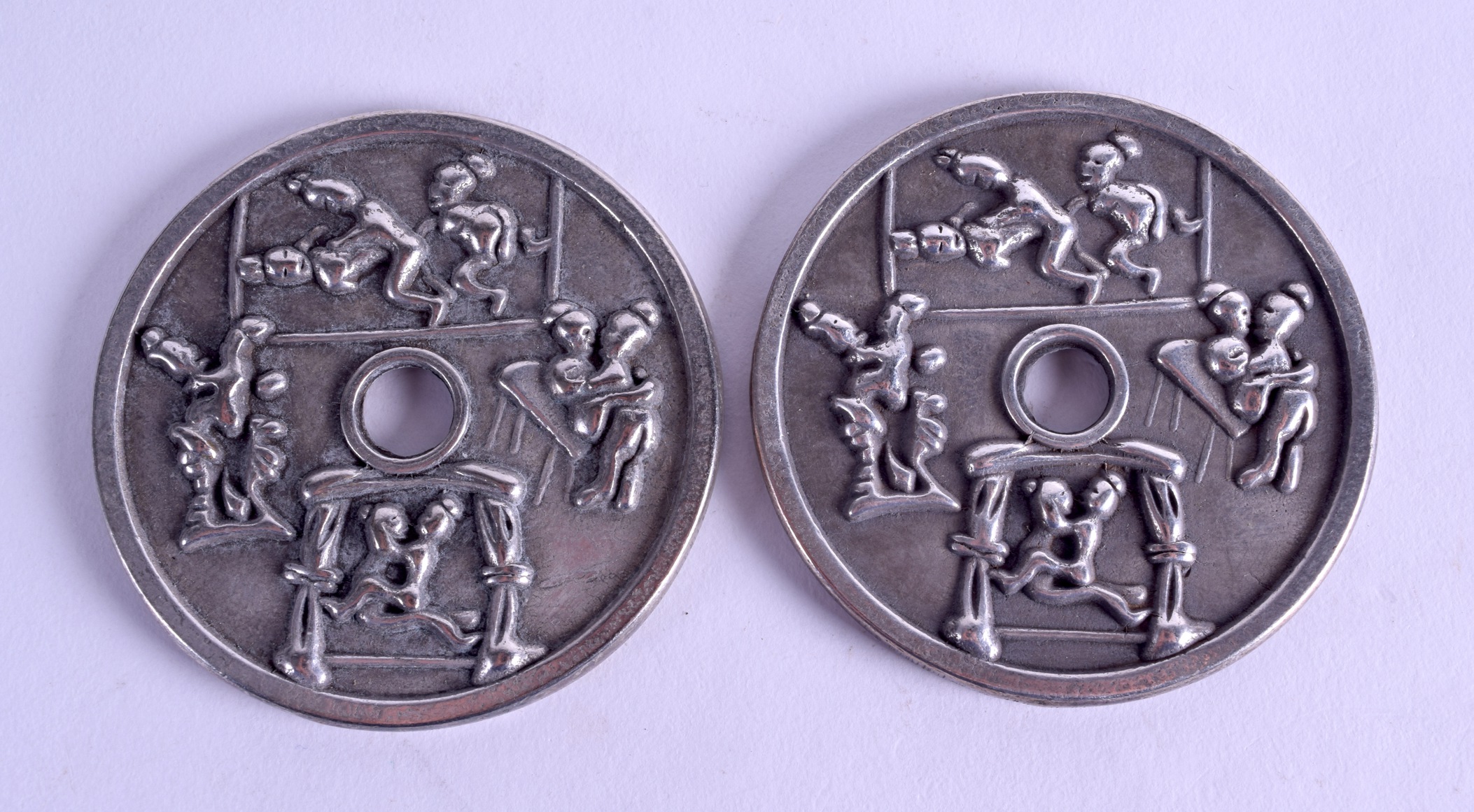 A PAIR OF CHINESE WHITE METAL CIRCULAR COINS decorated with figures in erotic pursuits. 7 cm