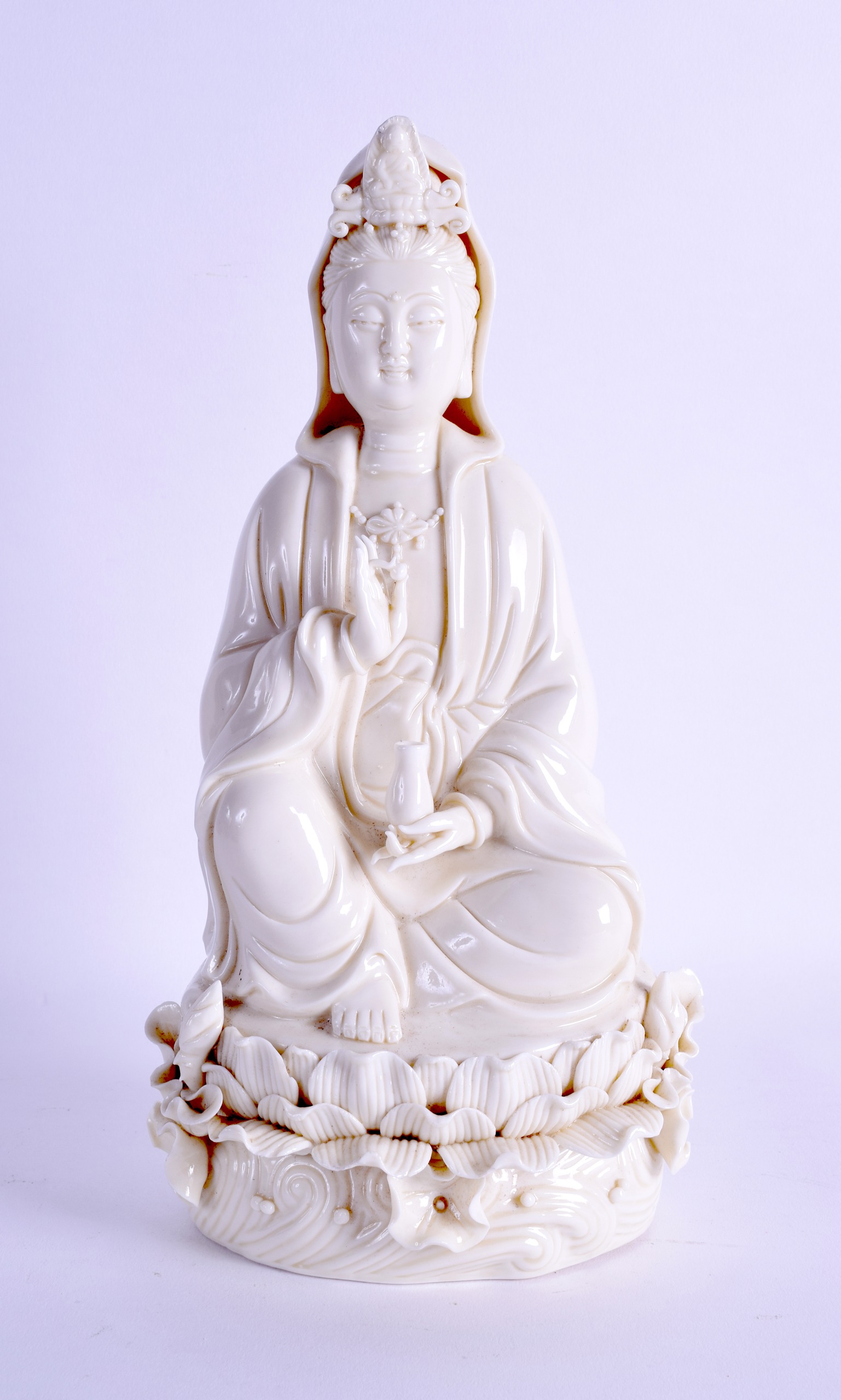 A CHINESE BLANC DE CHINE FIGURE OF GUANYIN modelled holding a vessel upon a lotus base. 27 cm high.
