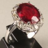 A RUBY AND DIAMOND CLUSTER RING, the oval facet cut ruby of approximately 7cts claw set to a