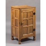 A ROBERT THOMPSON ADZED OAK BEDSIDE CUPBOARD of canted oblong multi panel form, the moulded edged