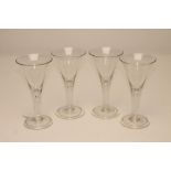 A SET OF FOUR WINE GLASSES, the trumpet bowls issuing from tear drop stems on a circular folded