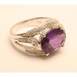 AN AMETHYST AND DIAMOND COCKTAIL RING, the oval facet cut amethyst claw set to a border and open