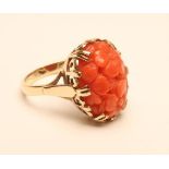 A DRESS RING, the oval coral panel carved and pierced with flowerheads on a plain 9ct gold shank,