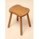 A ROBERT THOMPSON ADZED OAK STOOL of waisted rounded oblong form, raised on four splayed faceted and
