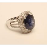 A SAPPHIRE AND DIAMOND CLUSTER RING, the oval cut sapphire of approximately 6.75cts claw set to a