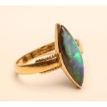 A BLACK OPAL RING, the marquise shaped cabochon polished stone open back collet set to beaded