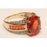 A FIRE OPAL COCKTAIL RING, the oval facet cut stone claw set to wide shoulders each channel set with