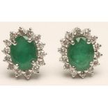 A PAIR OF EMERALD AND DIAMOND CLUSTER EAR STUDS, the oval facet cut emeralds claw set to a border of