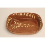 A LARGE SLIPWARE BAKING DISH of plain rounded oblong form with cream slip feathered border,