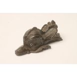 A BRONZE CLIP, 19th century, cast as a stylised dolphin with glass eyes, the foliate back plate with