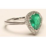 AN EMERALD AND DIAMOND CLUSTER RING, the Colombian tear cut emerald claw set to a border of numerous